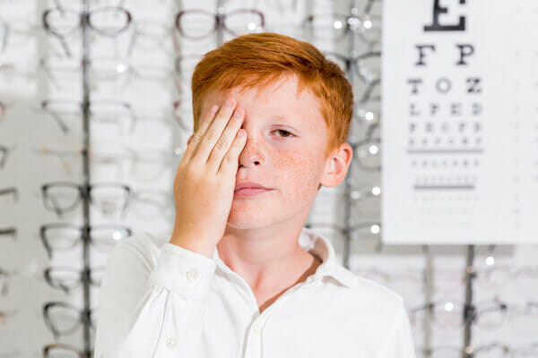 cute-boy-covered-his-eye-with-hand-standing-optics-clinic (1)
