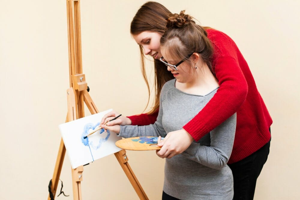 side-view-woman-helping-girl-with-down-syndrome-paint